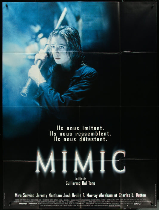 One-panel French movie poster for the film 'Mimic', featuring a dark tone with an image of a child holding a candle, text in French, and the movie title.