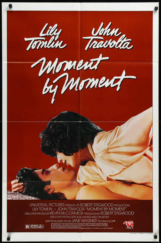 Vintage style movie poster featuring a man and a woman in an intimate pose against a red background, with the title 'Moment By Moment' written above in bold, white letters. The poster is folded and shows some wear.