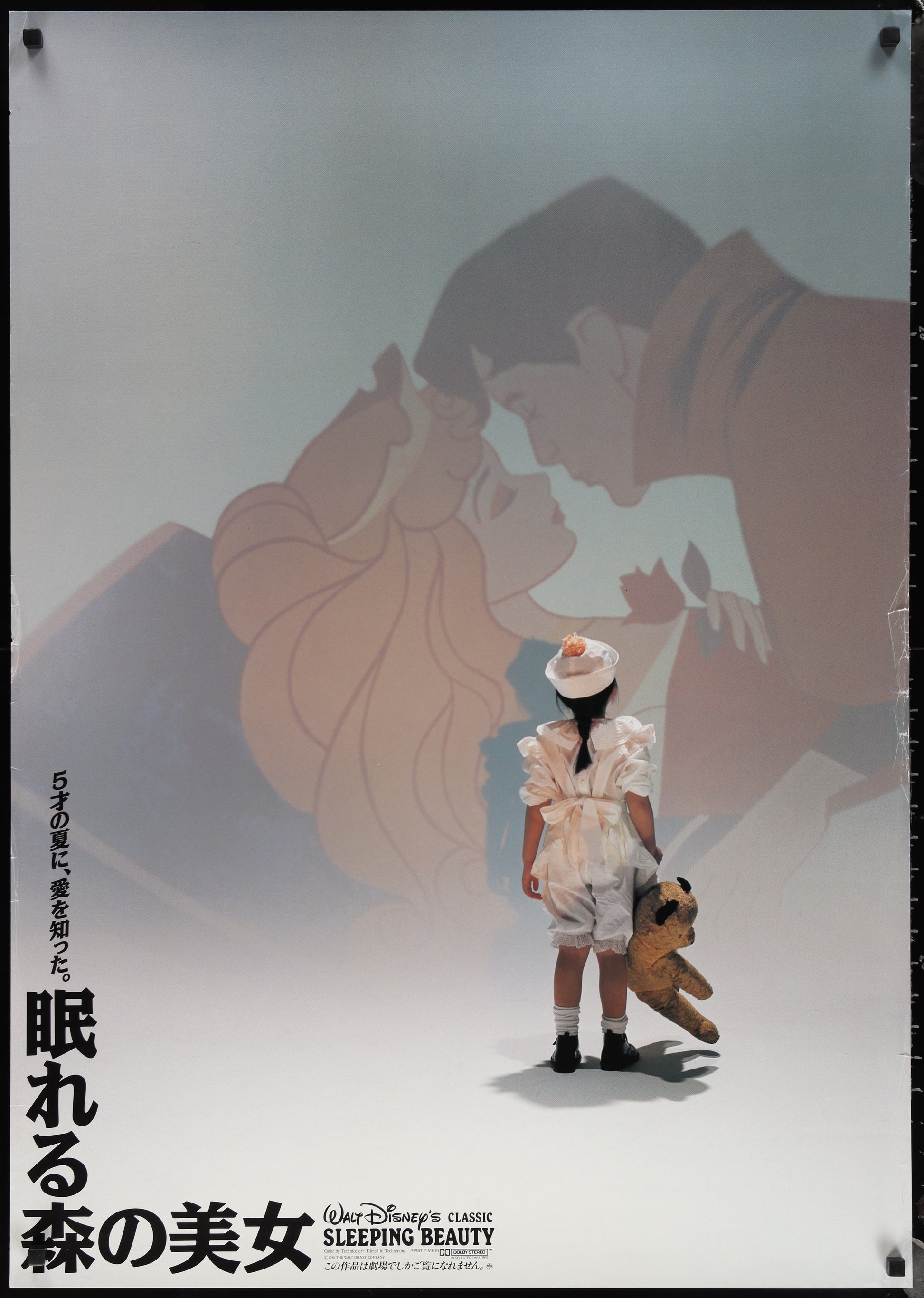 Person holding a teddy bear in front of a projection of 'Sleeping Beauty' with Japanese text.