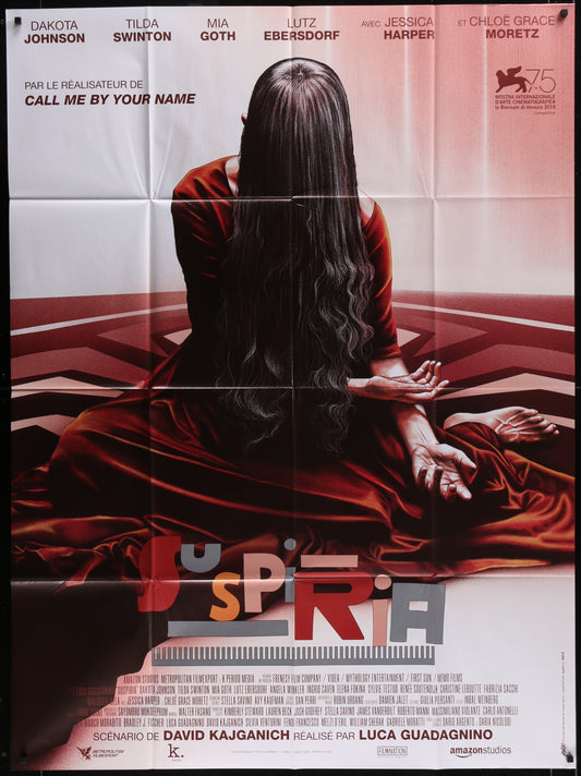 A movie poster for 'Suspiria' featuring a female figure in a red dress with a blurred background, indicating a horror genre.