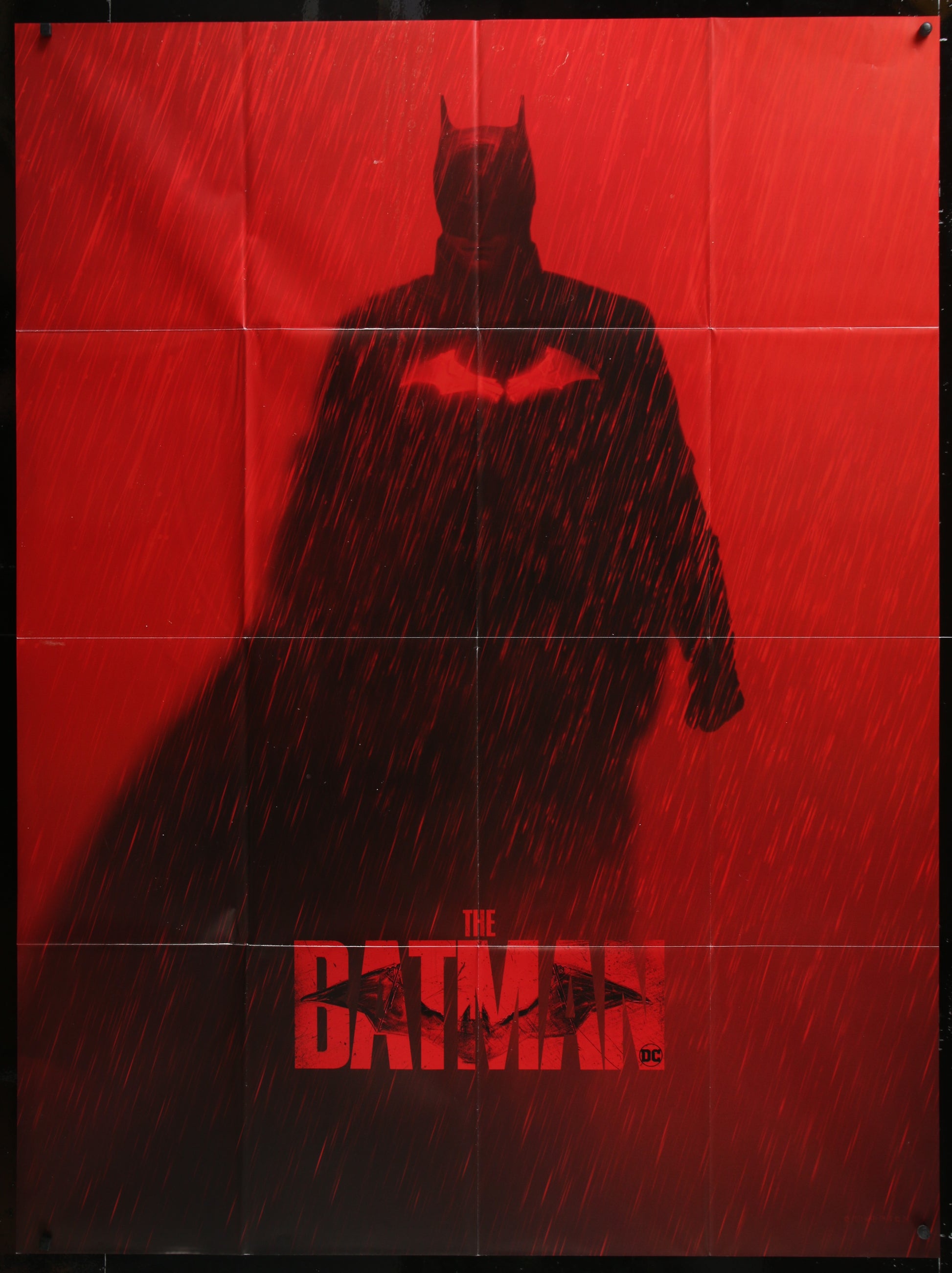 Dark silhouette of a superhero in a cape against a red background with 'The Batman' logo.